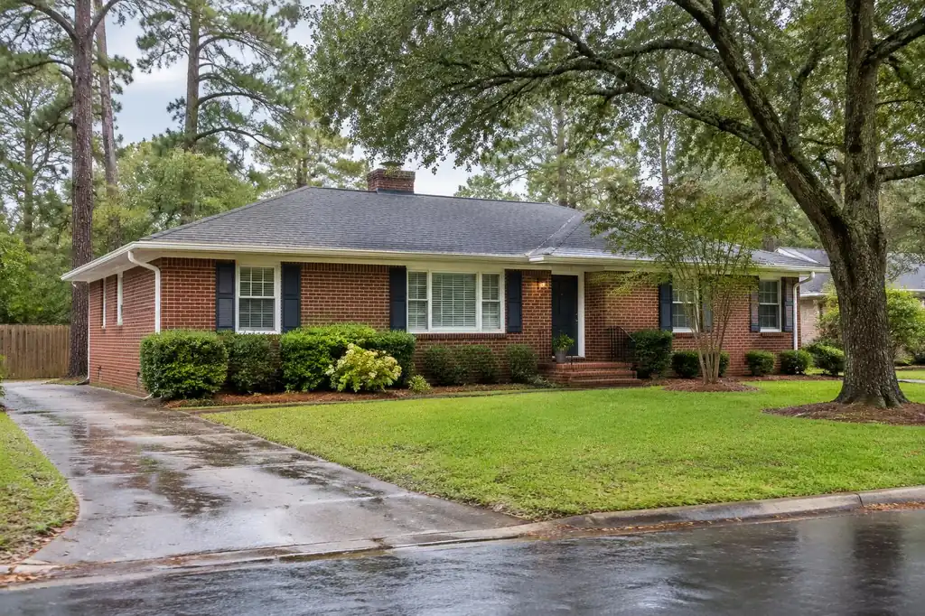 Brick ranch home with gutters under mature pine and oak trees